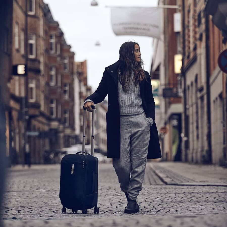 THULE Subterra Carry On Spinner pushed by woman on cobbled street