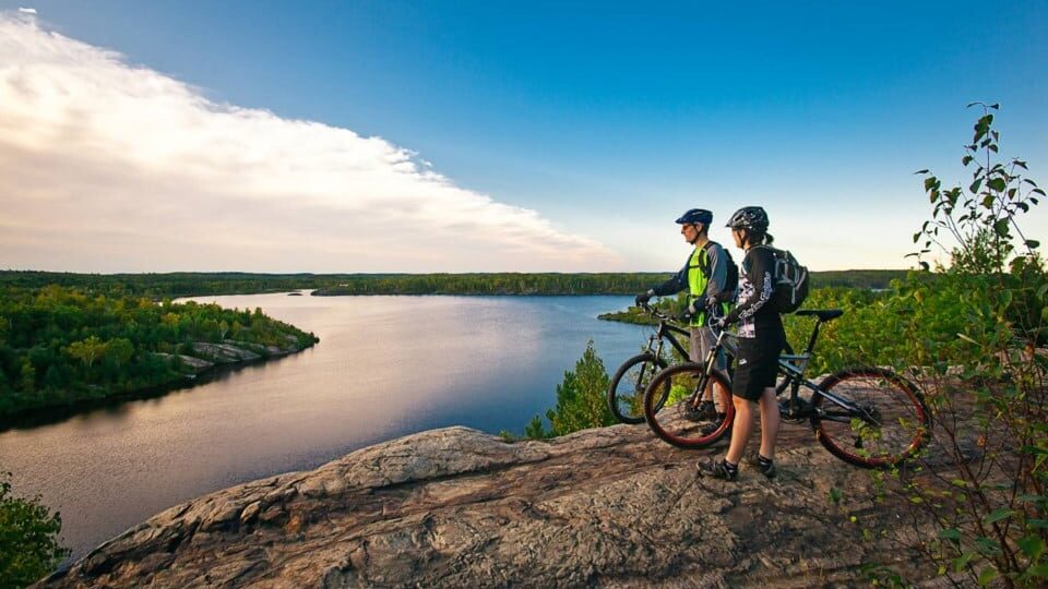 Two cyclists cycling in ontario, on a road near a lake